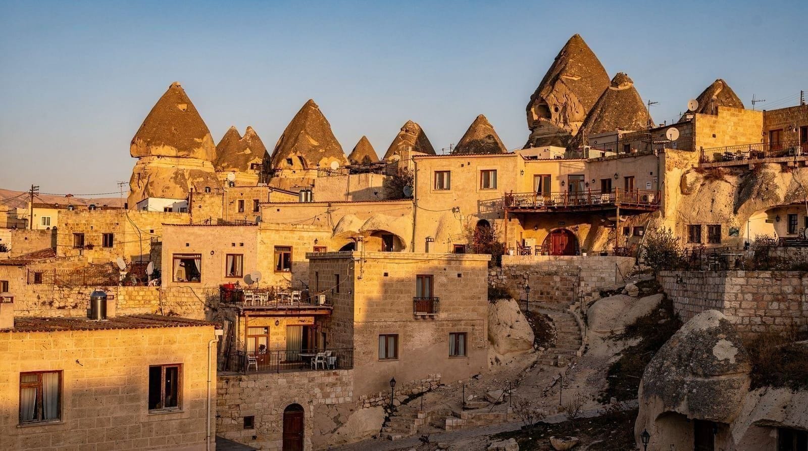 Feenkamine und Heißluftballons über Göreme im Morgenlicht, mit den Tälern Kappadokiens am Horizont.